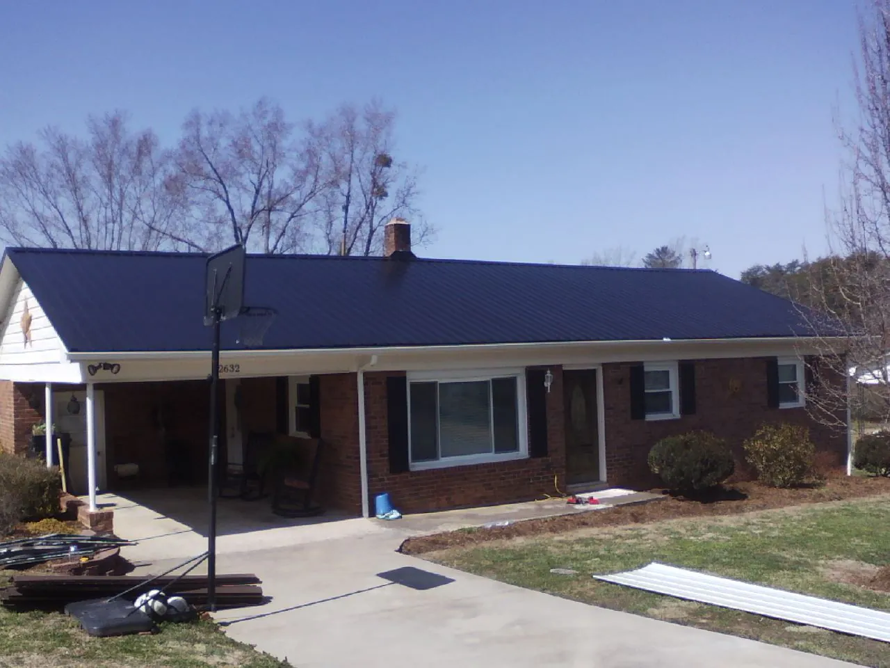 Finished dark blue metal roof on a brick ranch with a carport in Waco