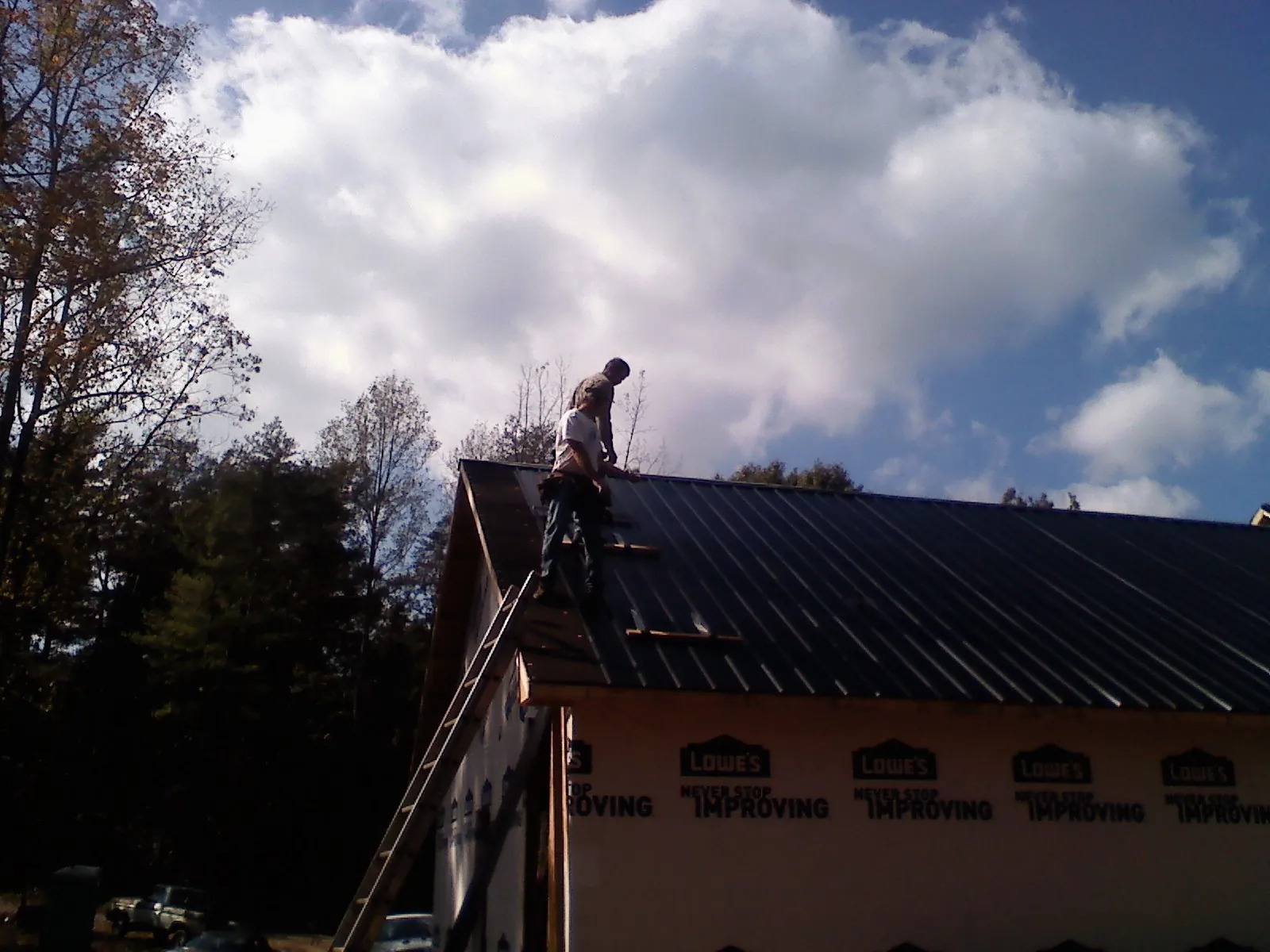 Roofer fastening dark metal panels high against a cloudy sky, from a Roof Inspection job in Waco